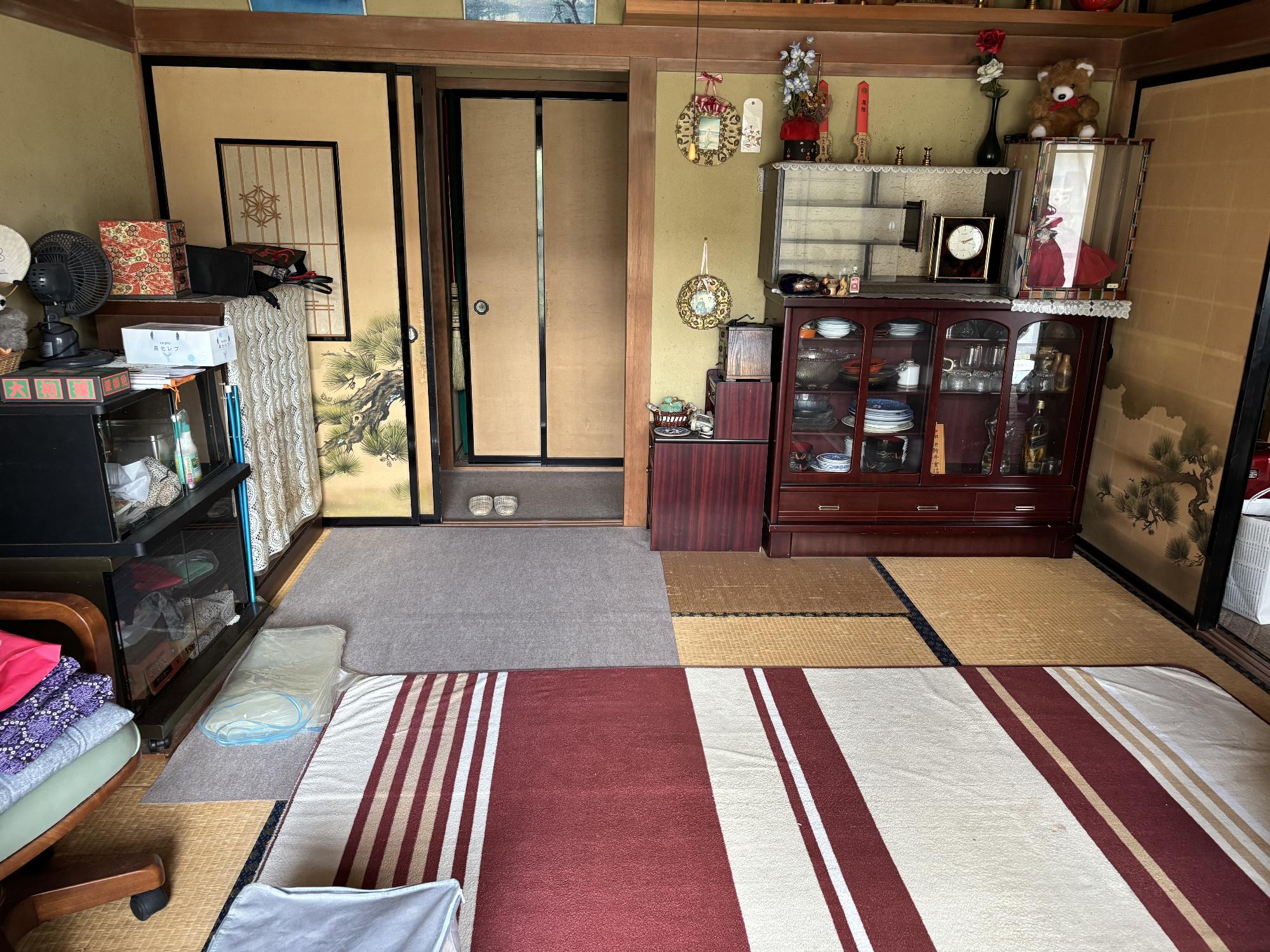 左側に物入、正面奥右側に食器戸棚、正面奥左側に襖引き戸、畳の上にカーペットが引かれている8帖和室の内観写真