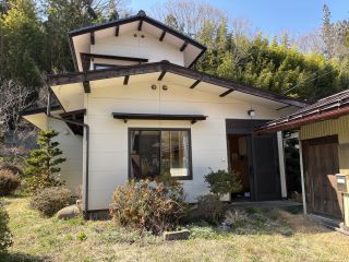 亜鉛メッキ鋼板・かわらぶきの白い建物で、右側に物置がある木造2階建て建物の外観写真