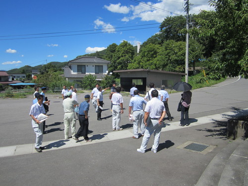 通学路で書類を持ってる男性や警察官など大勢の人たちが道路の先を指さしながら話をしている様子の写真