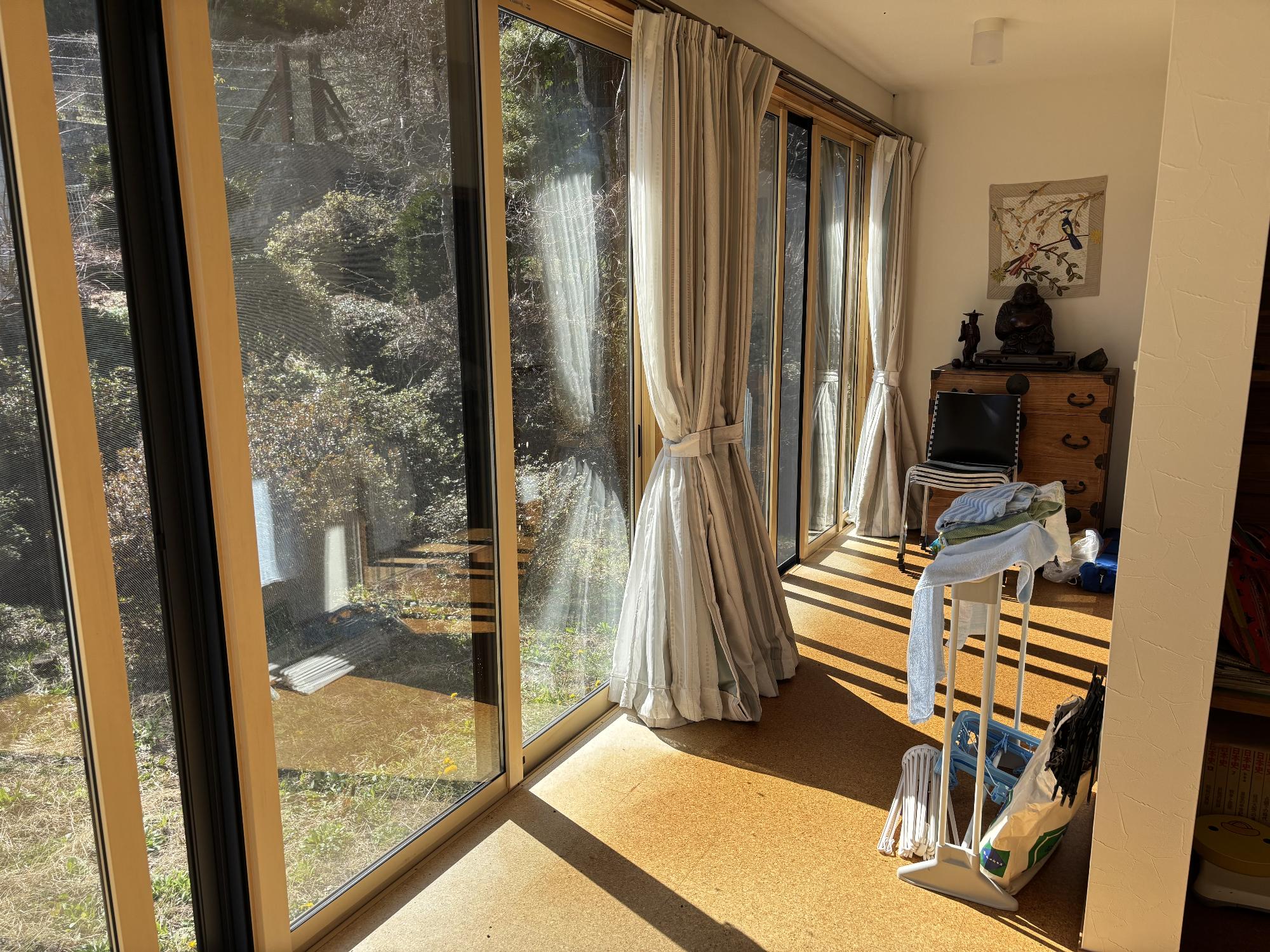 左側にカーテンを開けてあるアルミサッシ戸、正面奥に家具、右側手前にタオルが干してある、縁側内観の写真