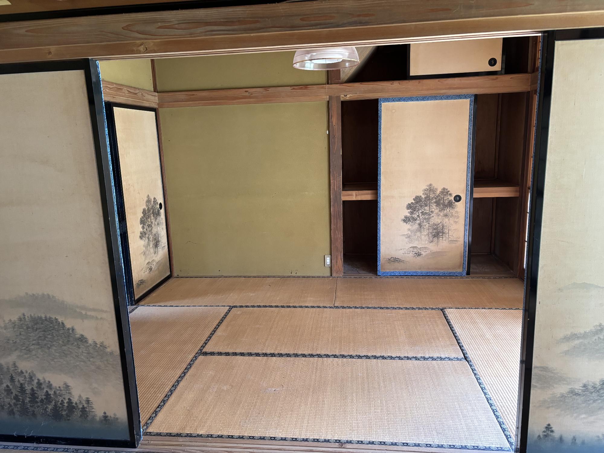 正面奥左側に押し入れ、左側に襖、正面中央上部に照明器具ある6帖和室内観の写真