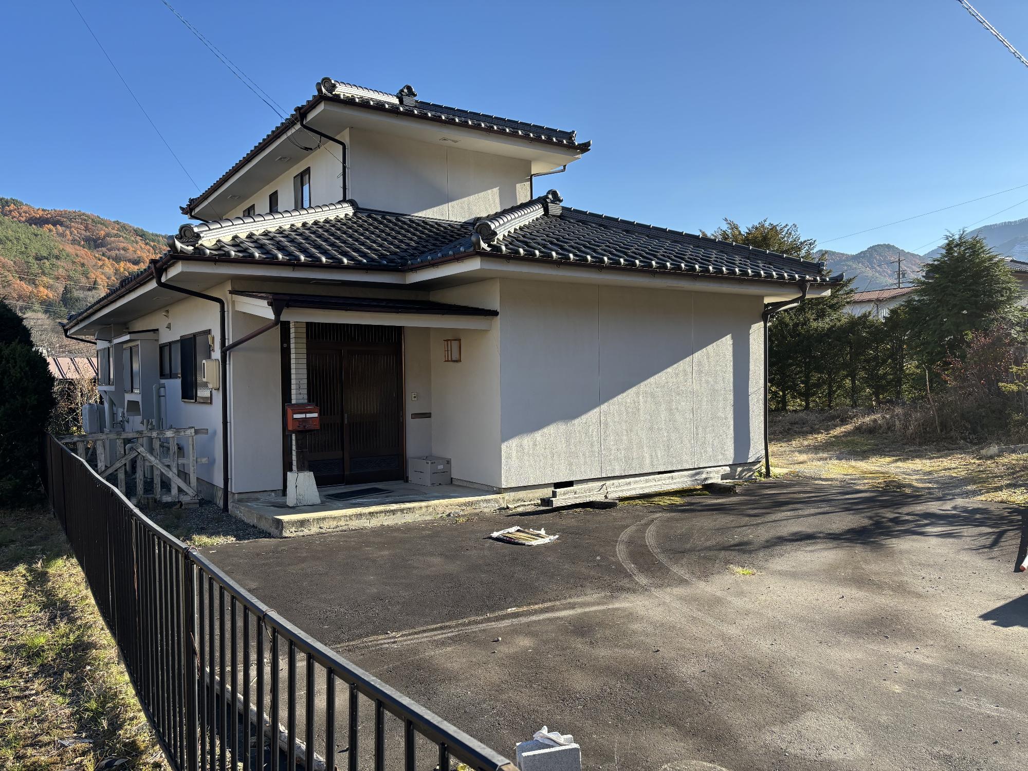 日本瓦屋根の白い建物で、左側にフェンスがある木造2階建て建物の外観写真