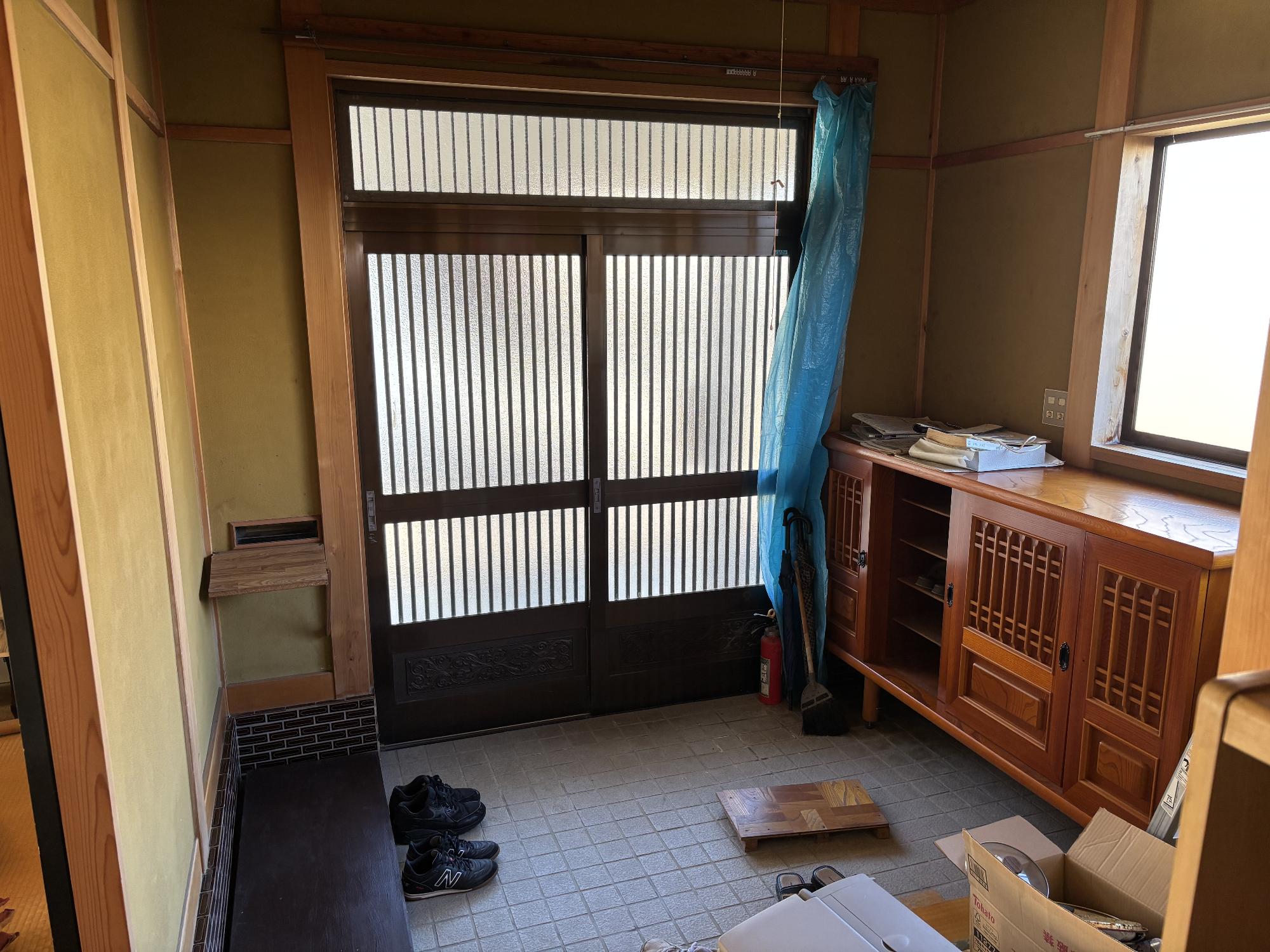 正面中央にアルミ玄関サッシ、右側に下駄箱、その上に曇りガラスサッシ、左側に踏み台がある玄関内観の写真