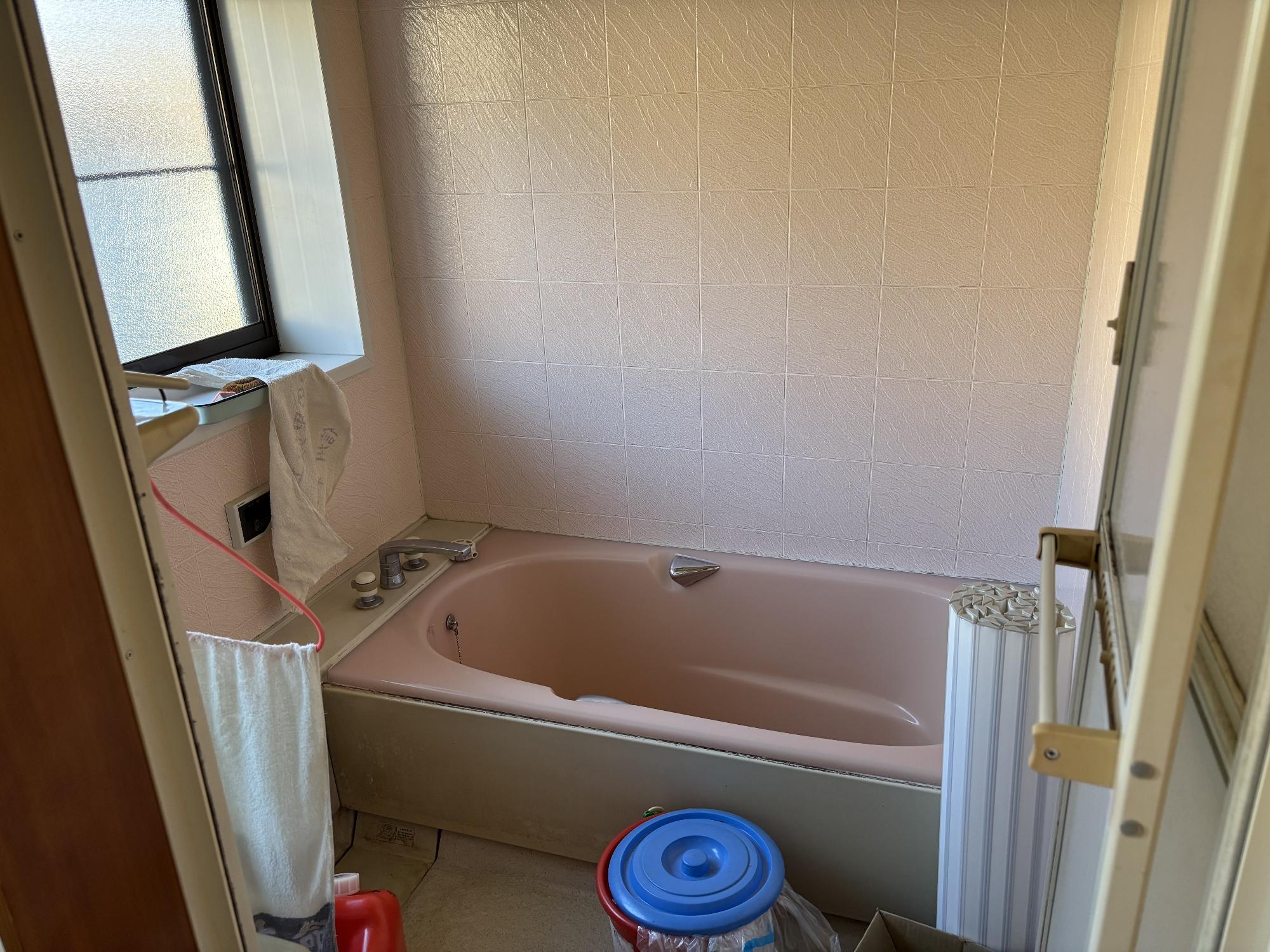 正面奥に浴槽、左側にリモコン、タオルが干してあり、その上部に曇りガラスアルミサッシ、右側に浴槽蓋を丸めて置いてあるシステムバスの浴室の写真