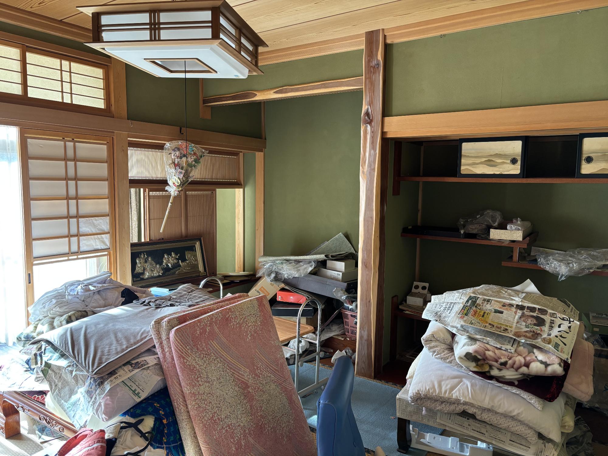 正面奥に床の間、左右手前に布団を乗せた座卓、左側に雪見障子戸、上部に照明器具がある8帖和室の内観写真