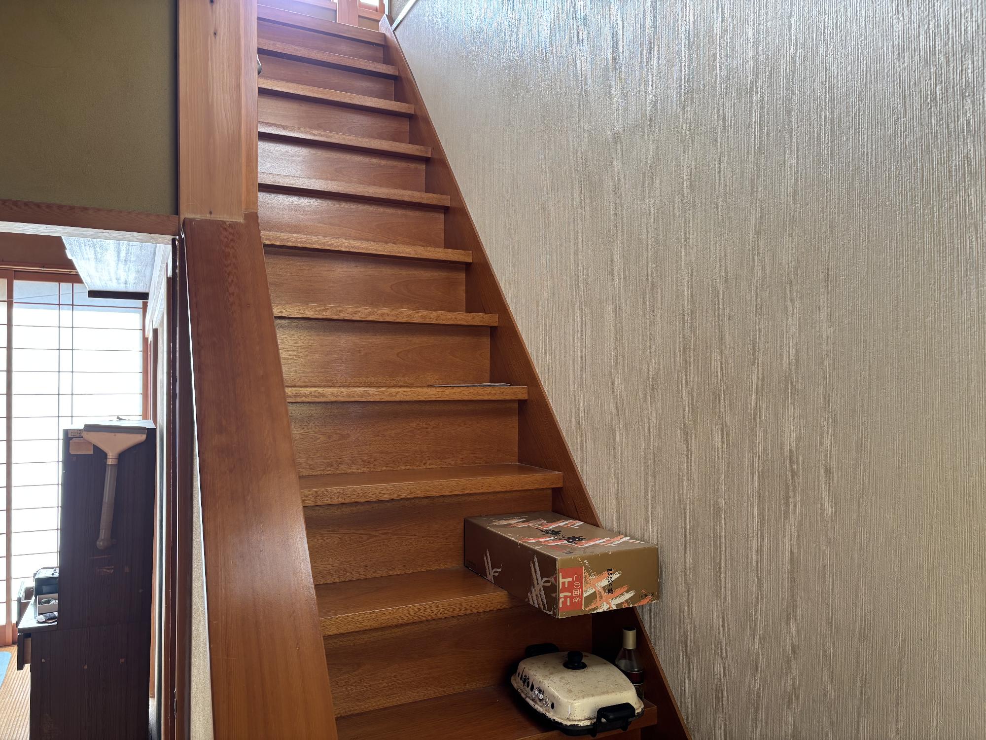 右側に壁、正面左側に手擦り、手前に荷物が置いてある階段内観の写真
