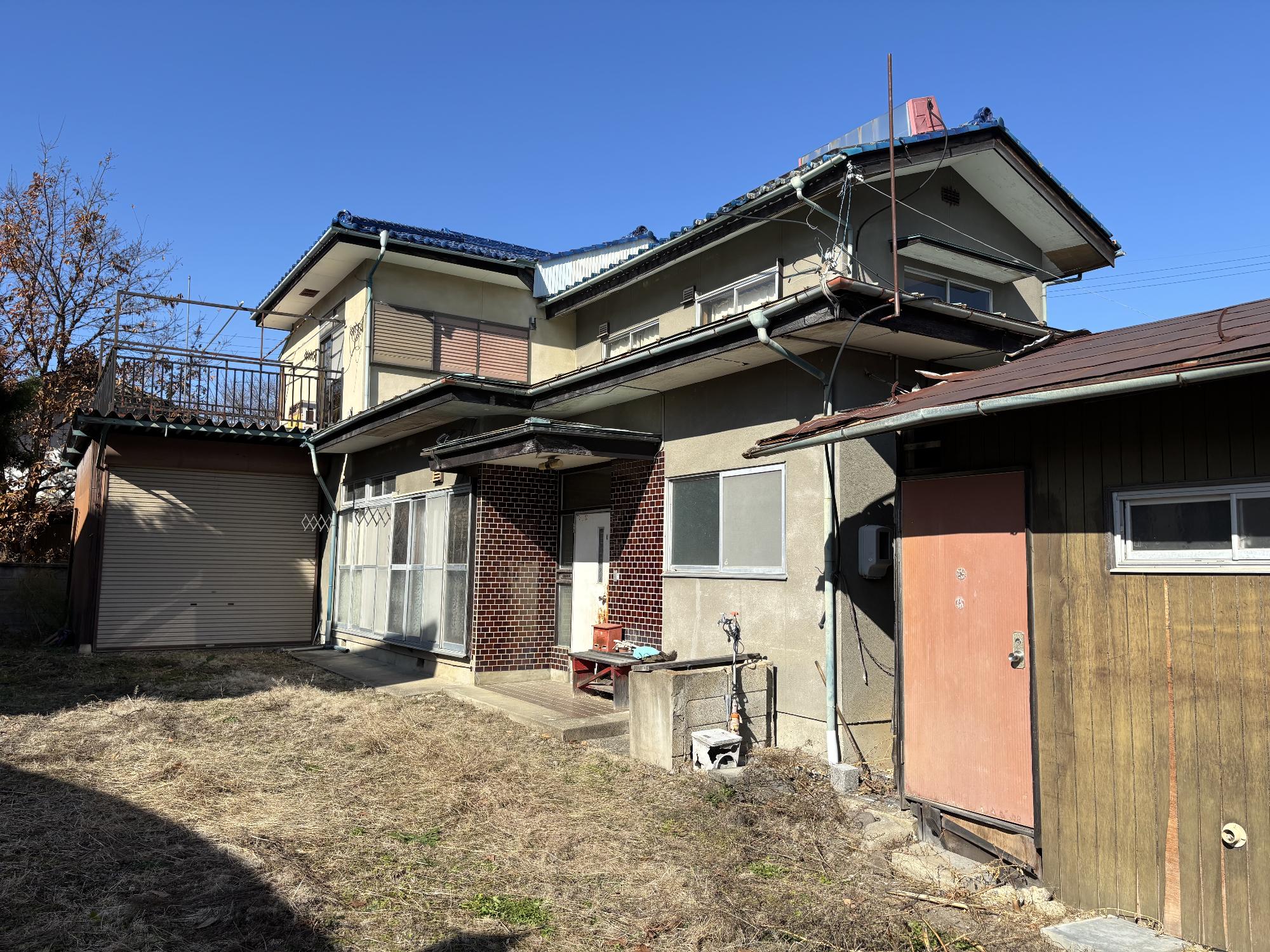 日本瓦屋根の白い建物で、2階屋根にはベランダがある木造2階建ての建物の外観写真