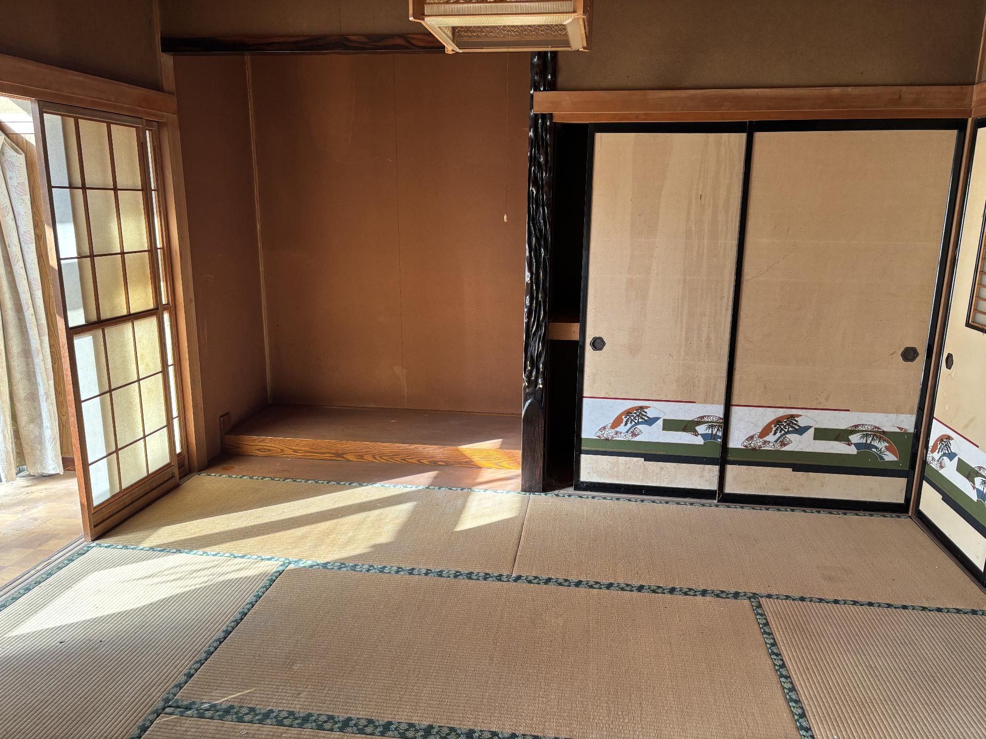 正面奥に床の間、右側に襖、左側に雪見障子、正面上部に照明器具がある、1階6帖和室の内観写真