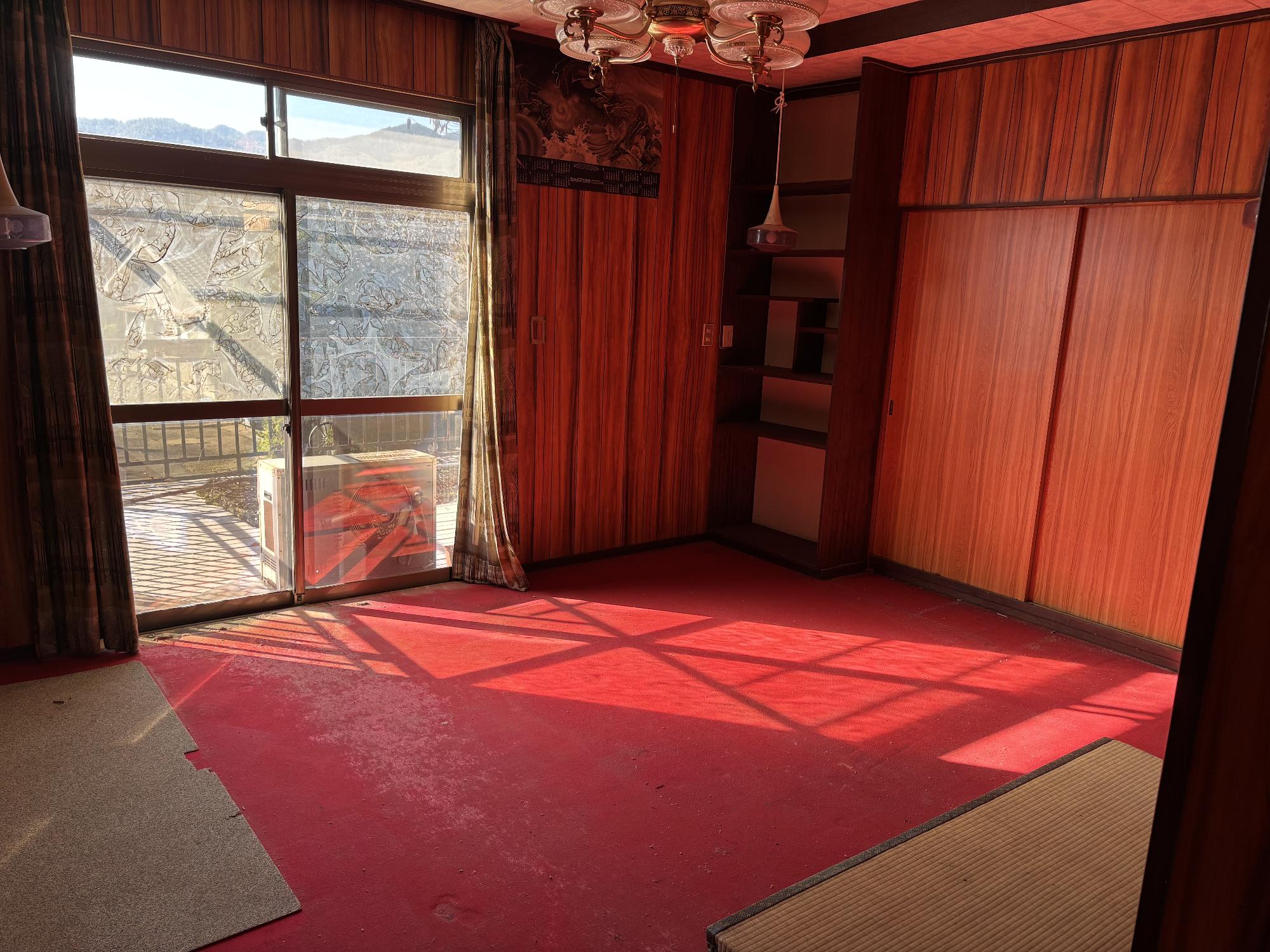 左側奥にアルミガラスサッシ戸、右側奥に物入収納壁、正面中央上部に照明器具、手前にカーペットが引かれている、2階10.7帖洋室内観の写真