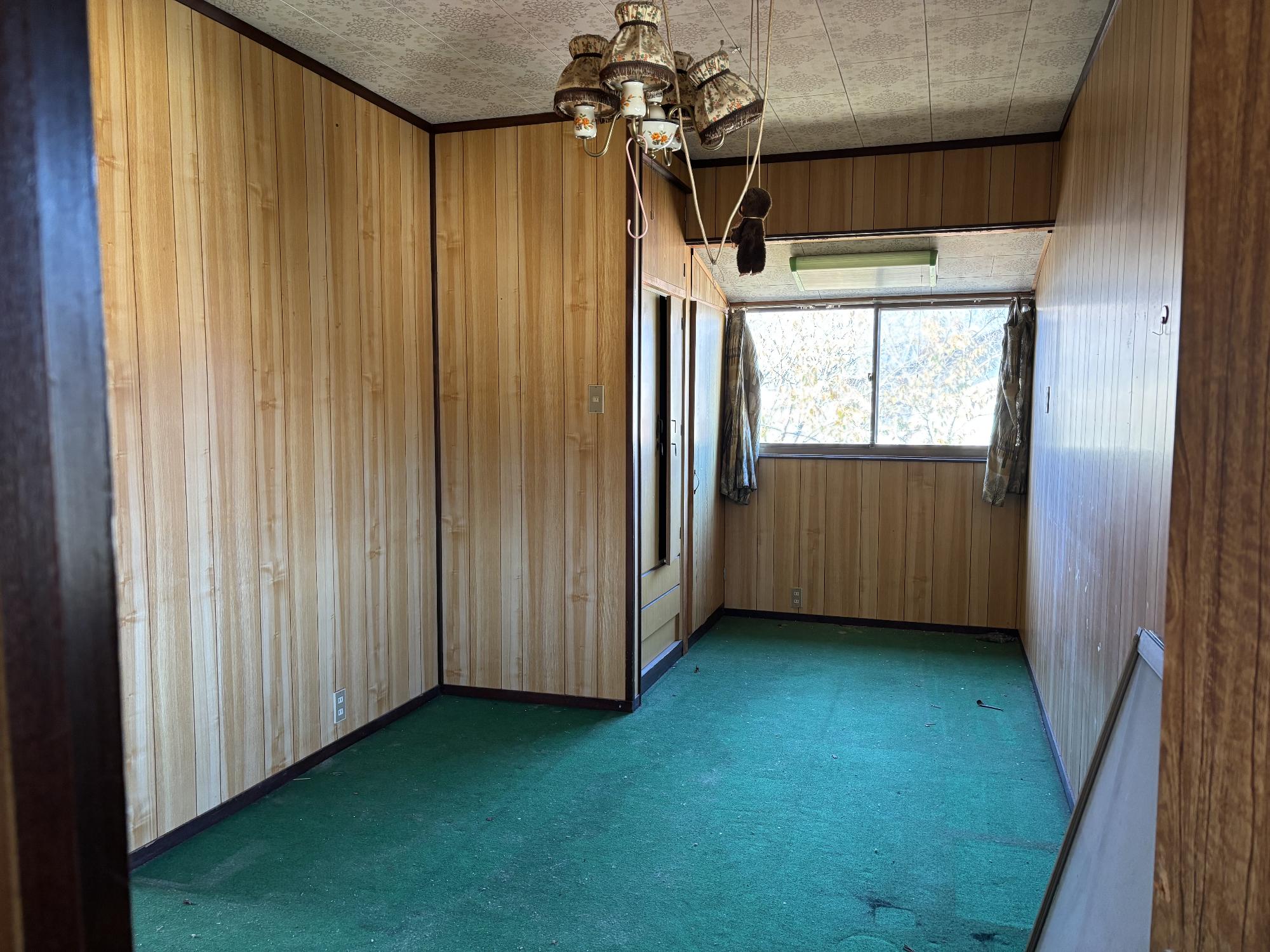 正面奥中央にアルミサッシガラス戸、その左右に開いたカーテン、正面中央上部に照明器具、手前に青いカーペットが引いてある2階7.5帖洋室内見の写真