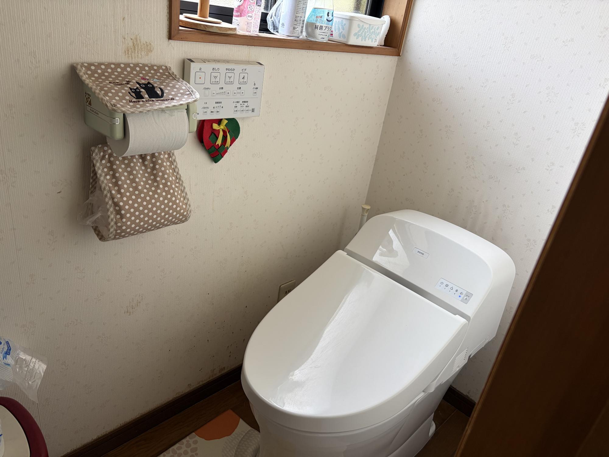 正面手前に洋式便座、左側にリモコン、トイレットペーパーホルダーがある、トイレの写真