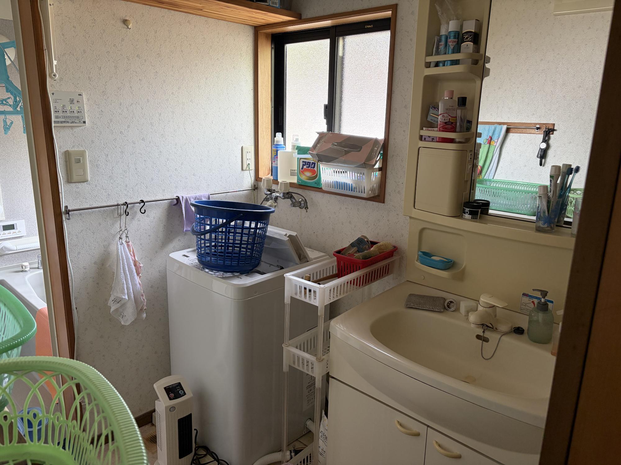 正面奥に洗濯機、右側に収納ミラー付洗面台、正面奥上部にアルミ曇りガラスサッシ戸がある、洗面所の写真