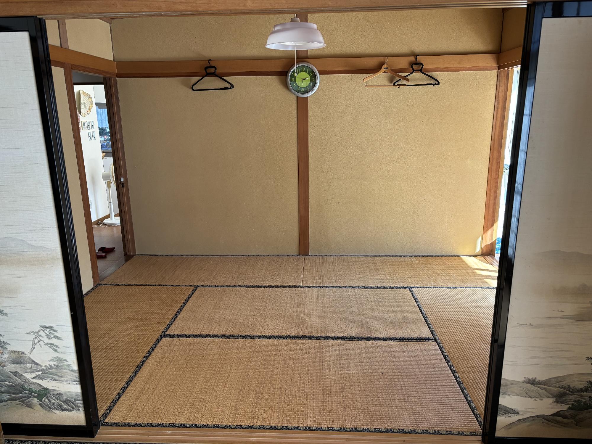 正面中央上部に照明器具、正面中央奥に掛け時計、その左右にハンガーが掛かっている、6帖和室内観の写真