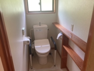 中央奥上部にサッシ、中央に洋式便座、その左右にトイレットロール、右側に物置スペースがあるトイレの写真